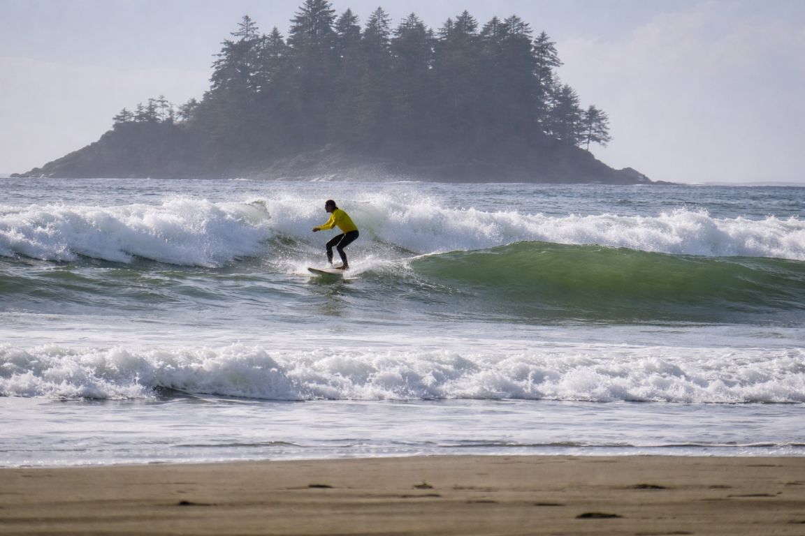 Surfer riding a wave at Chesterman Beach in Tofino with island backdrop during a tour with Tofino Tour Packages